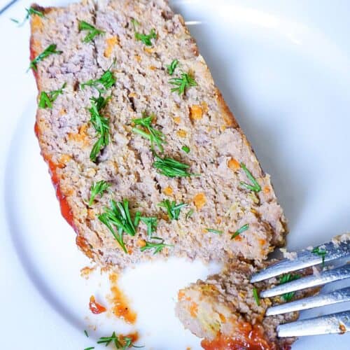 A slice of turkey and beef meatloaf sprinkled with green herbs on a white plate.