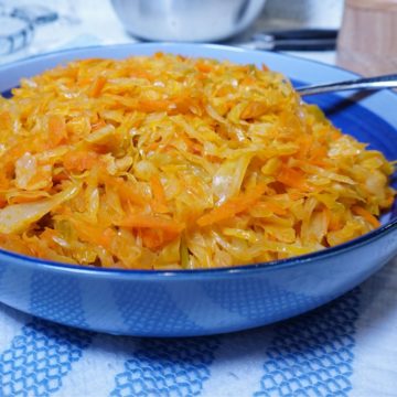 Cooked shreds of cabbage and carrots in a blue plate. The plate is placed on a striped blue and white kitchen towel.