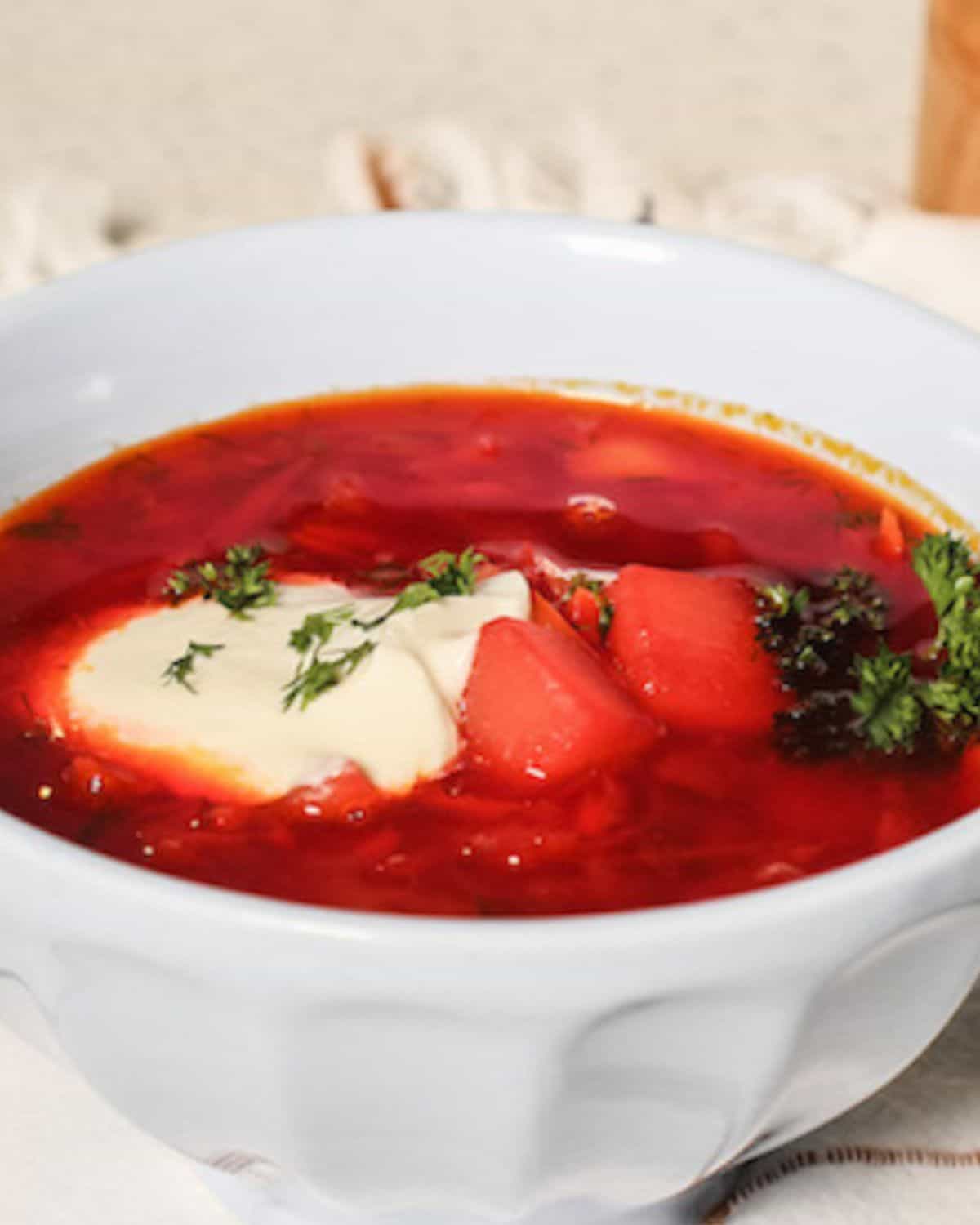 A light blue bowl with a red soup and some cream on top.