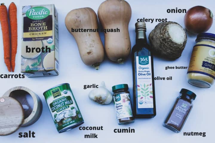 Laid out ingredients to make the squash creamy soup: carrots, broth, 2 butternut squashes, celery root, olive oil, onion, salt, coconut milk, garlic, cumin, ghee butter, nutmeg/