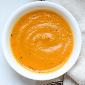 Creamy butternut squash soup served in a white bowl and garnished with black pepper on top.