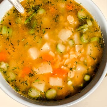 Split pea soup with asparagus served in a blue bowl. There are visible potatoes, carrots, asparagus and chopped green dill. the soup is yellow and chunky.