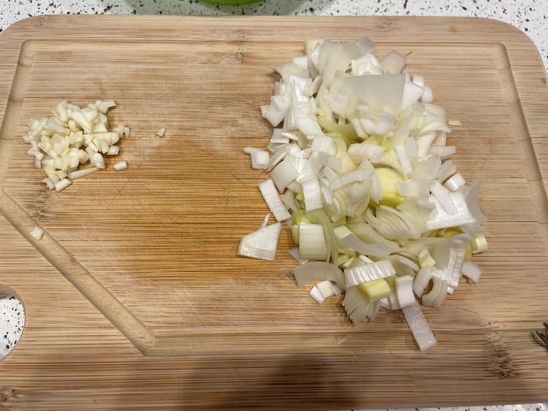 Finely chopped leek and garlic on a cutting board.