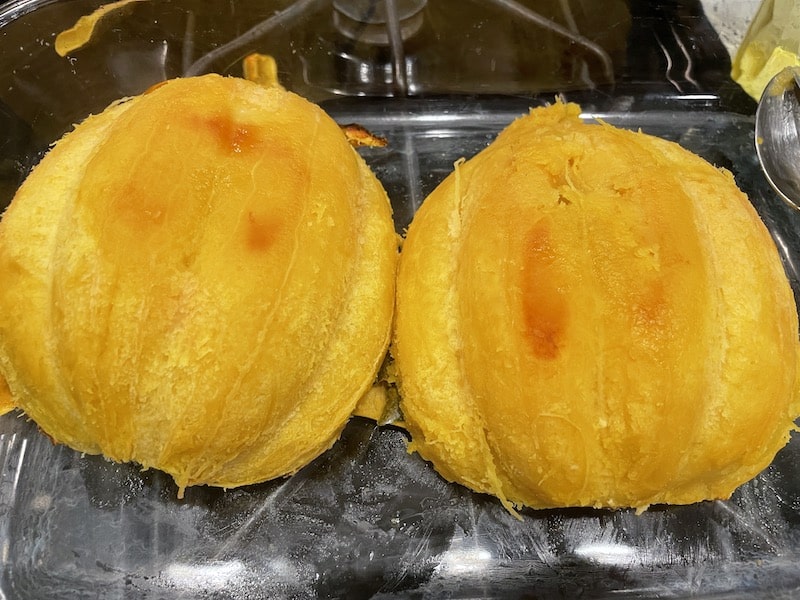 Two baked and peeled acorn squash halves on a glass dish with the cut side facing down.