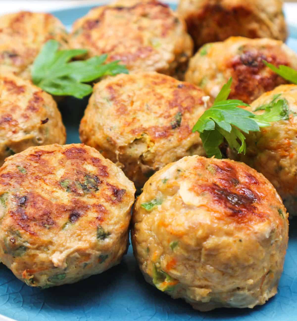 Cooked turkey meatballs are arranged on a blue plate. There are a few leaves of green parsley on top.