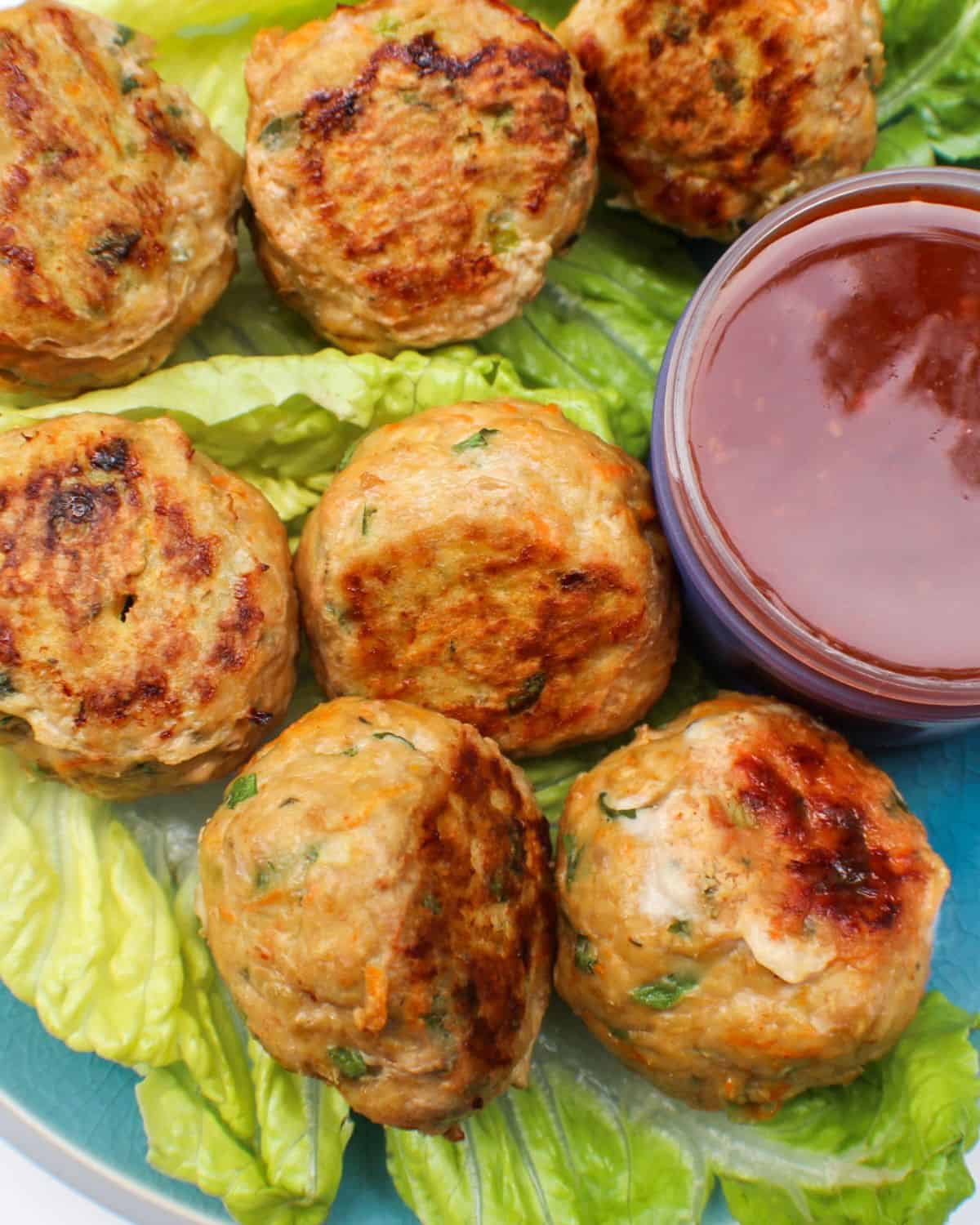 Browned meatballs on a green lattice leaf and a glass bowl with some red sauce on the side.