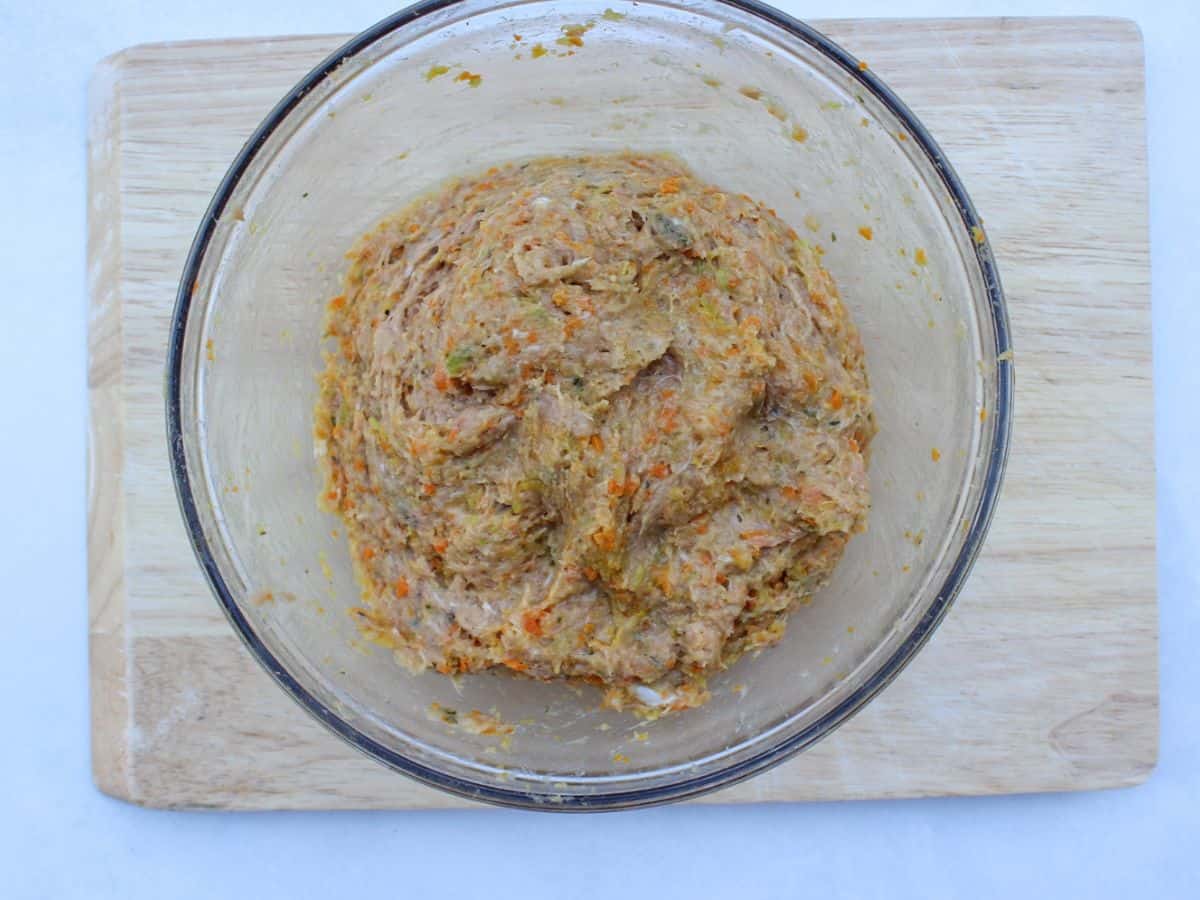 A large glass bowl on a wooden cutting board with the meat mixture on a wooden cutting board.