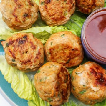 Browned meatballs on a green lattice leaf and a glass bowl with some red sauce on the side.