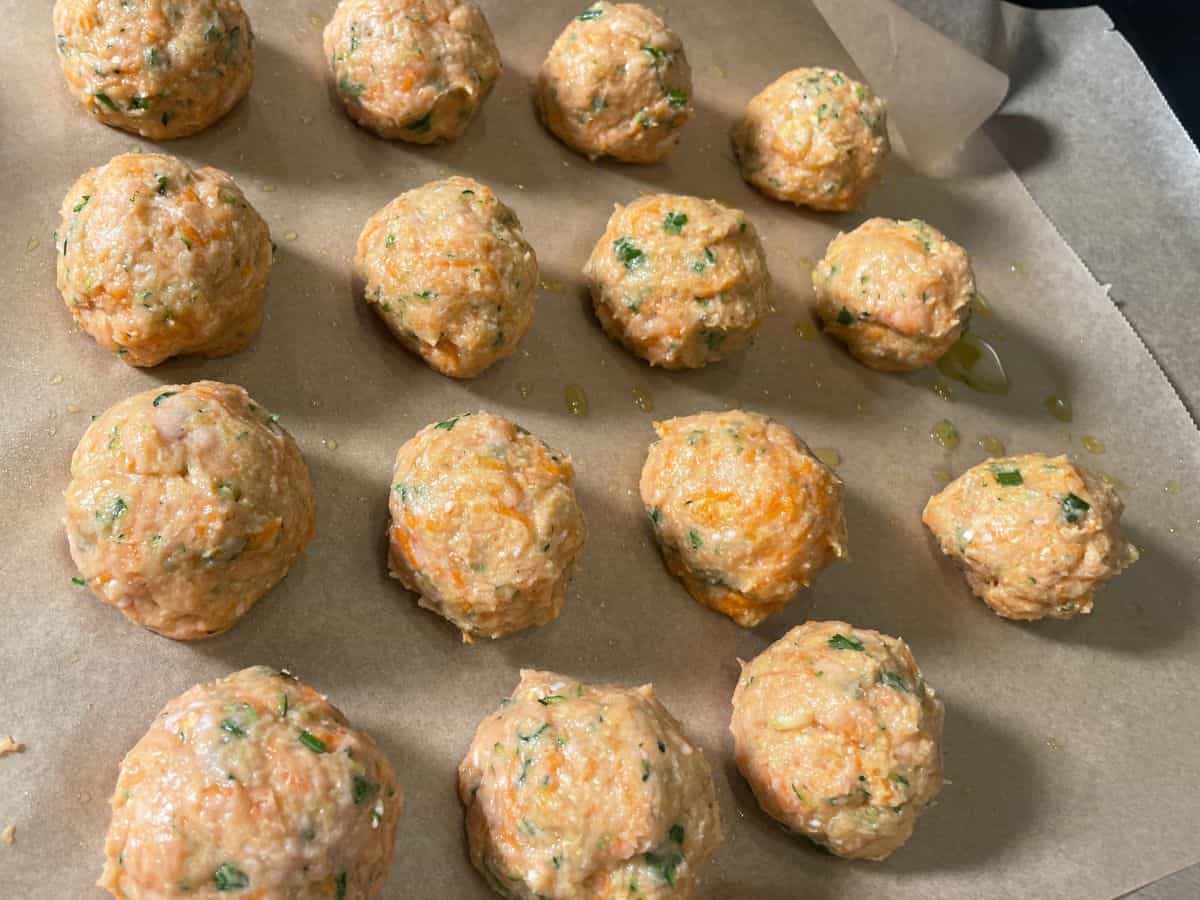 Formed raw turkey meatballs arranged on parchment paper.