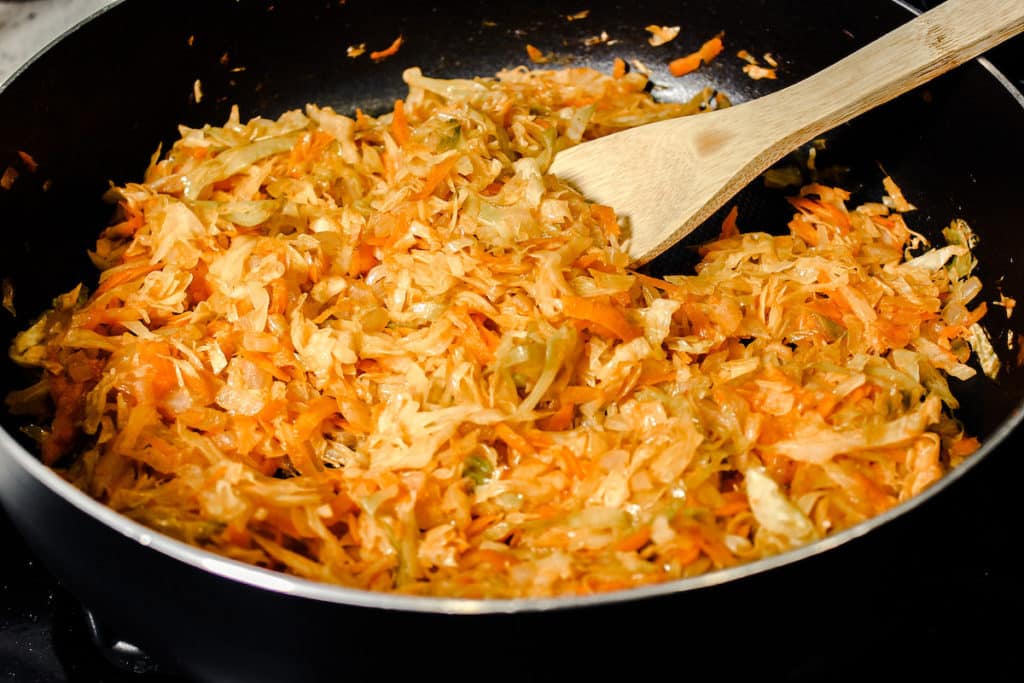 Shredded cabbage and carrots are being cooked in a frying pan. 