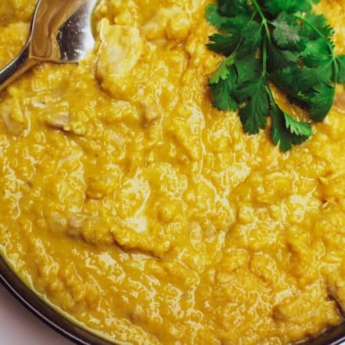 A bowl filled with yellow curry with red lentils and chicken garnished with fresh cilantro.