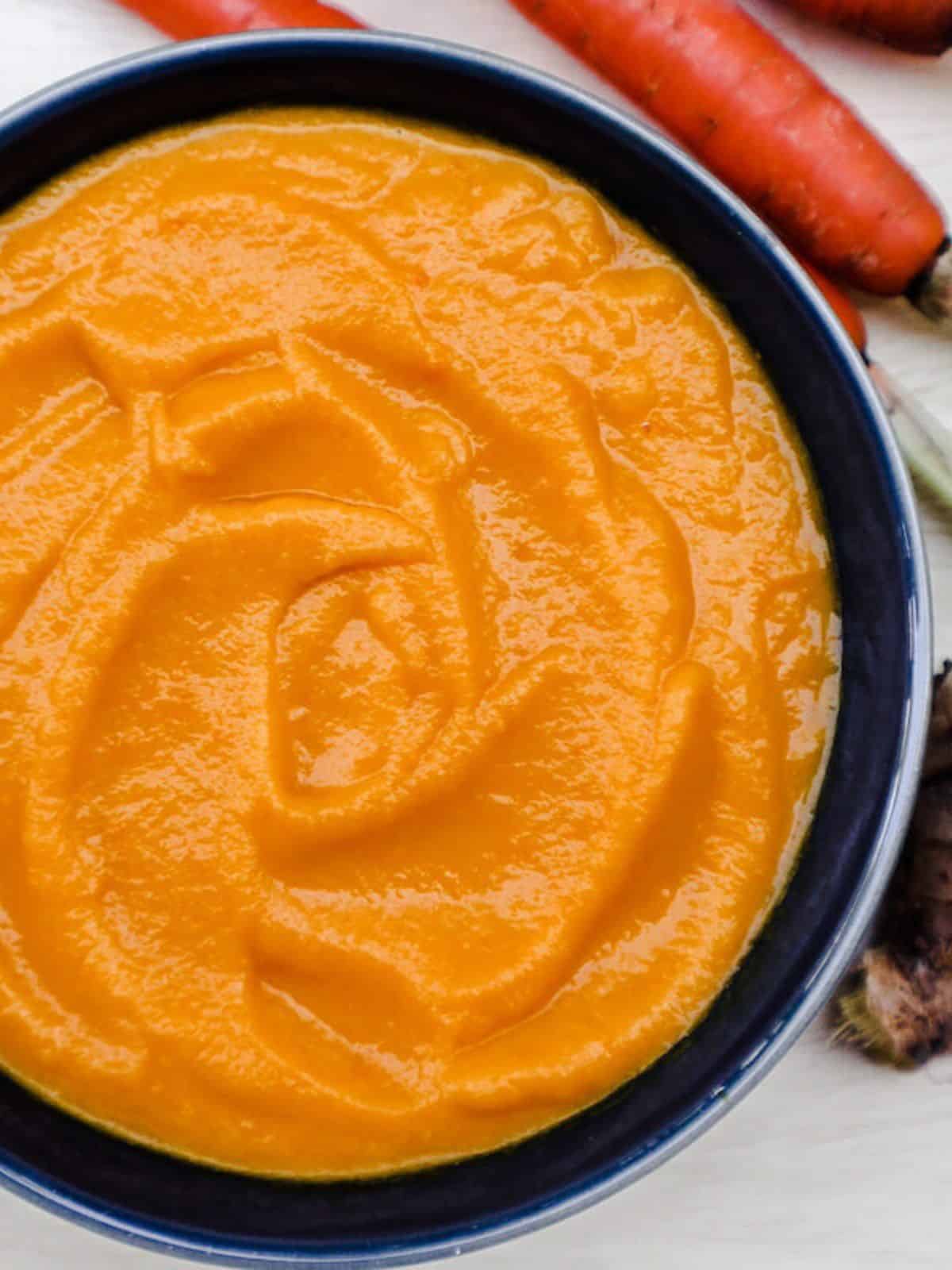 Orange creamy carrot soup in a dark bowl.