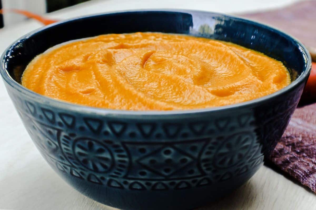 Side view of a dark blue bowl with carrot soup.