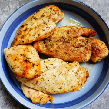 Golden cooked whole chicken breasts are on a large light blue plate.