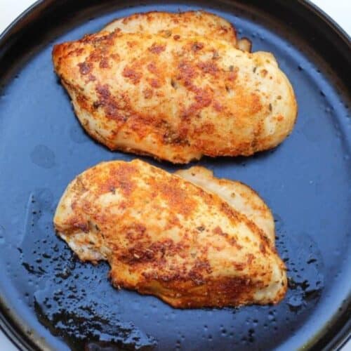 Two golden pan-fried chicken breast in a cast iron skillet.