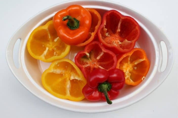 colorful raw bell peppers with tops cut off arranged in a baking dish