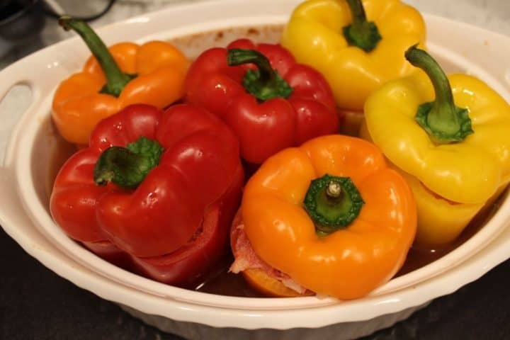 yellow, orange, red bell peppers stuffed with beef and rice arranged in a white baking dish.