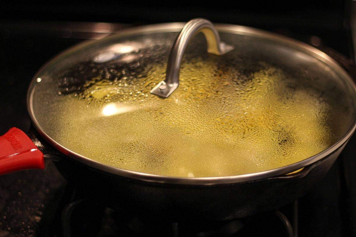 Potatoes and onions frying in a large pan covered with a lid. 
