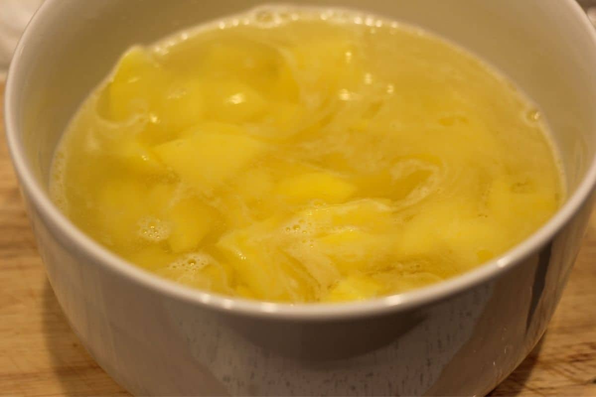 Sliced potatoes soaking in a bowl with cold water. 