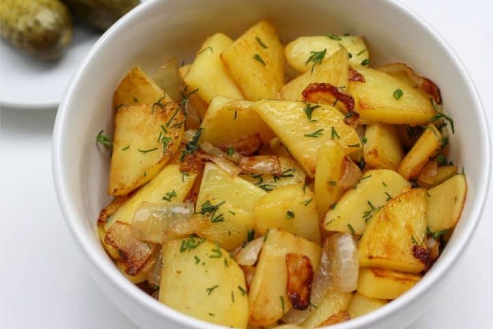 fried potatoes with onions, topped with fresh dill and pickels on a side
