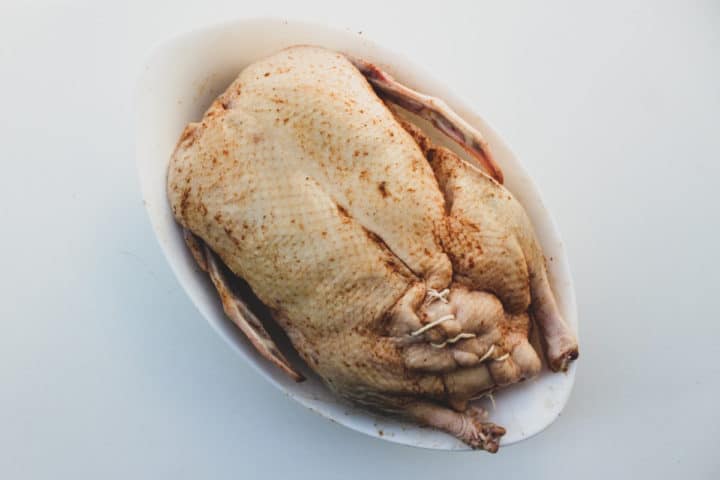 whole duck rubbed with spices placed in a white deep dish.