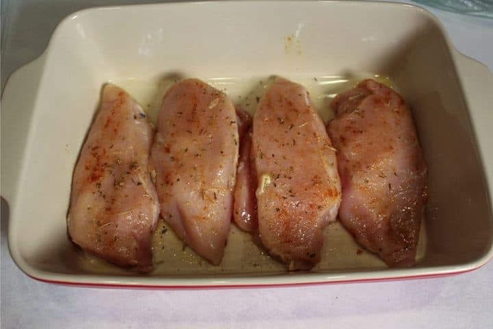 Four raw chicken breasts in the baking dish.