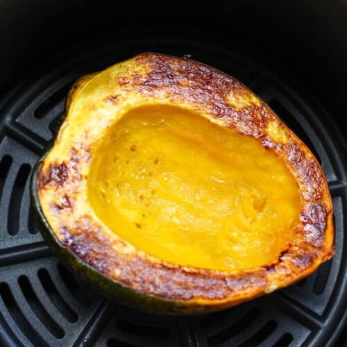 Golden brown squash half in air fryer basket facing the cut side up.