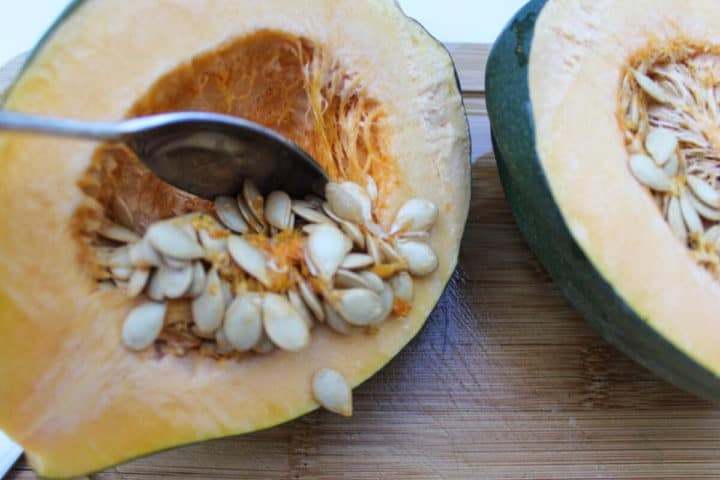 Cut in half acorn squash, seeds are being removed with the spoon.