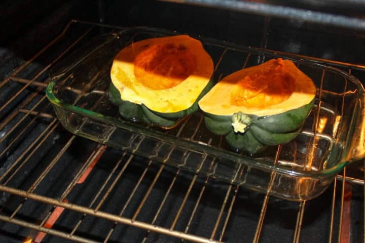 Two acorn squash halve in a baking dish placed in the oven rack. 