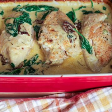 Creamy baked Tuscan chicken with spinach and sun-dried tomatoes served in a deep ceramic dish.