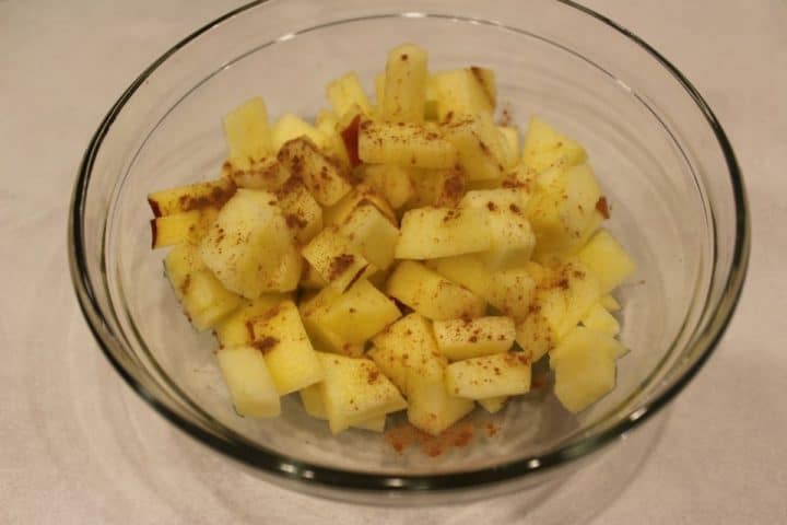 Peeled and cubed apples in a glass dish with some lemon juice and cinammon on top.