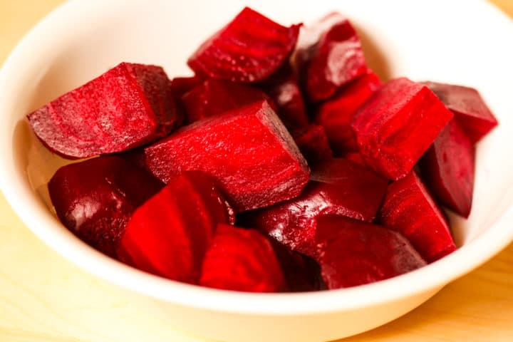 Cooked, peeled and cubed  red beets in a white bowl.