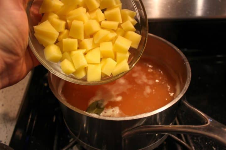 Chopped potatoes being added to the boiling pot of lentil soup.