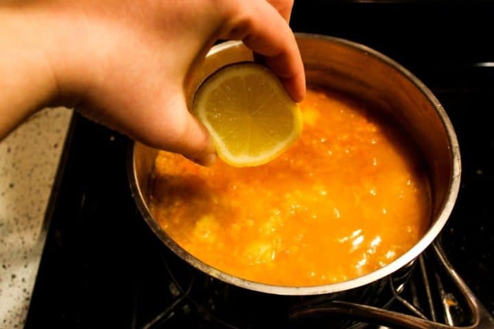 A hand squeezing some lemon juice into the soup.