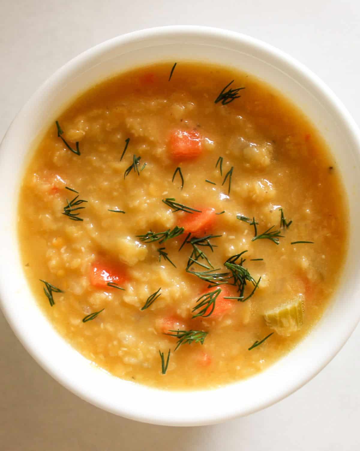 Lentil soup with chunky vegetables is served in a white bowl and topped with fresh green herbs.