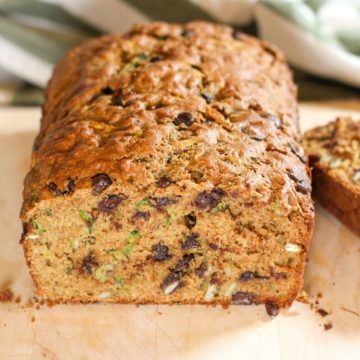 Zucchini bread with chocolate chips in a cutting board. The loaf is cut and showing the cut side on a shot.