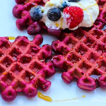 Feature image of the recipe: red beet waffles on a white plate, topped with yougurt and berrie and drizzled with liquid honey.