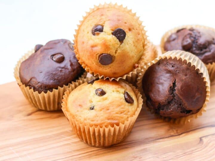 Soft muffins (vanilla and double chocolate) filled with chocolate chips on a cutting board.