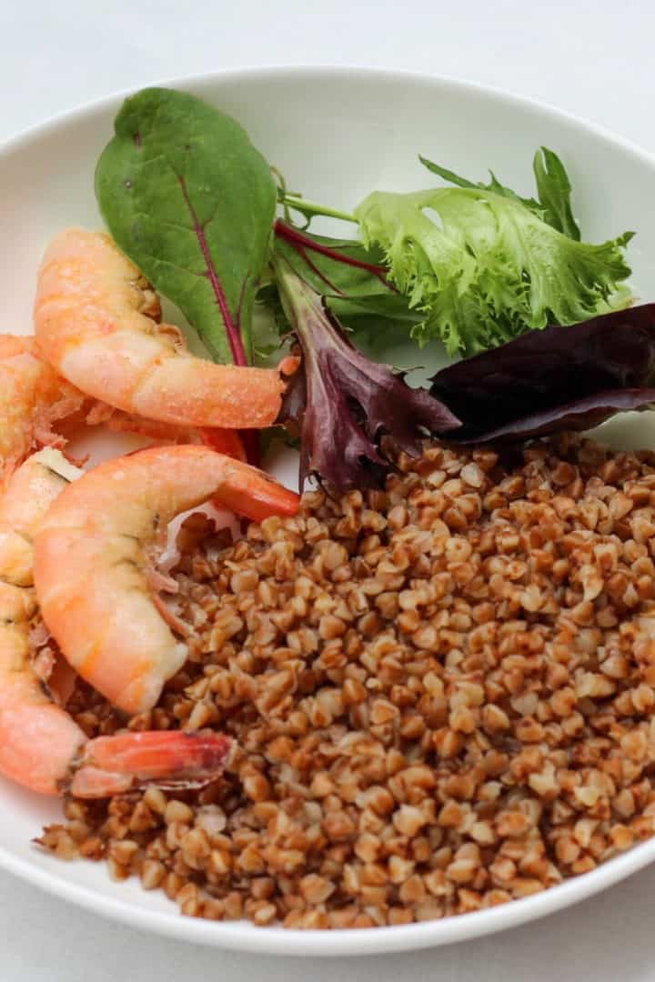 White plate with buckwheat, shrimps and a salad on the side