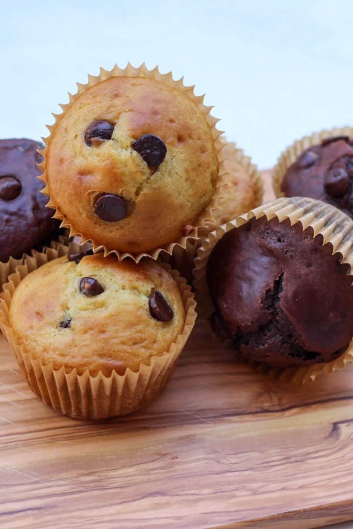 Vanilla and double chocolate muffins on a wooden board.