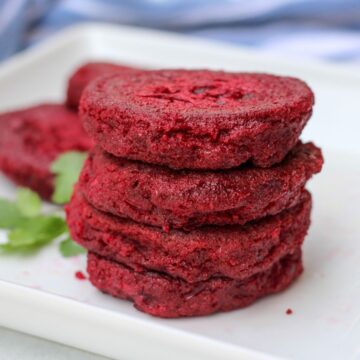 Four stacked red beet cutlets on a white plate.