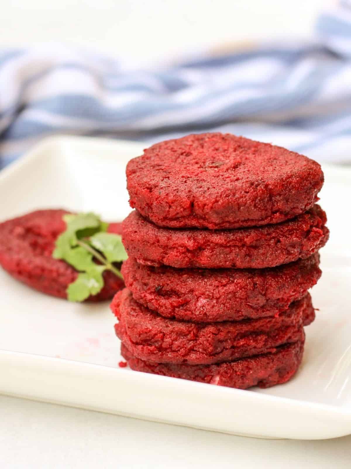 Red beetroot cutlets stacked on a whote plate with a sinlge cutlet and some green parsley visible behind.