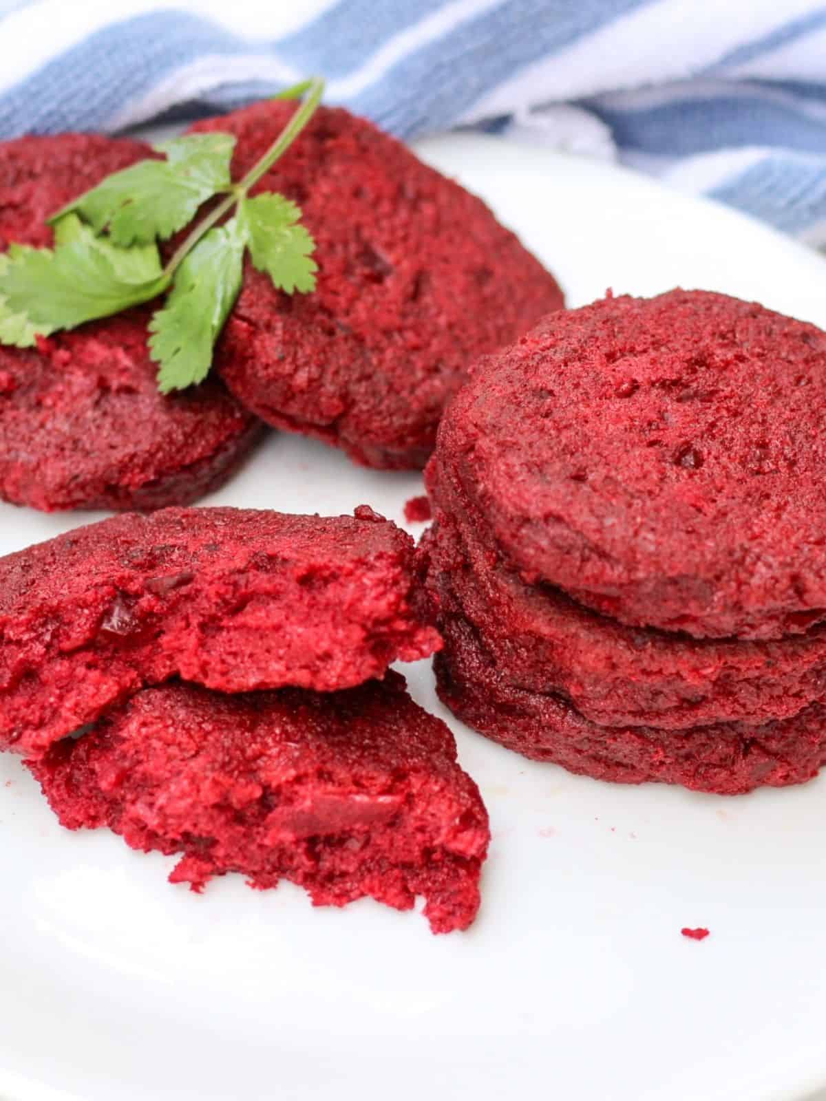 Red beet cutlets on a white plate with one broken in half to show how it looks inside.