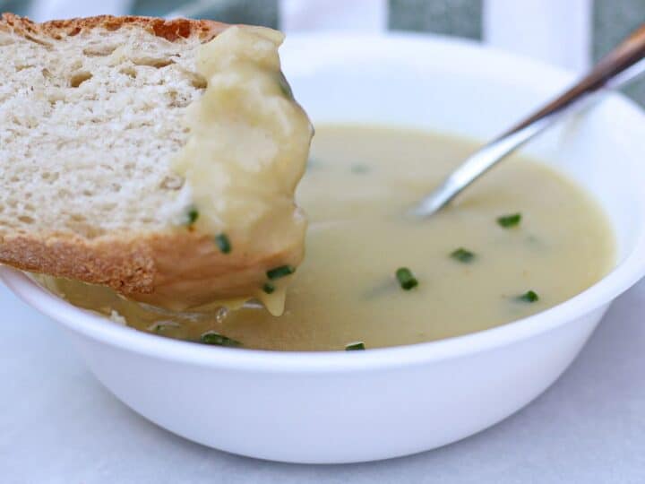 Slice of bread dipped into a bowl of creamy potato leek soup garnished with diced chives