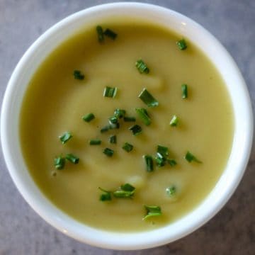 Overhead shot of creamy potato soup in a white bowl, garnished with chives.