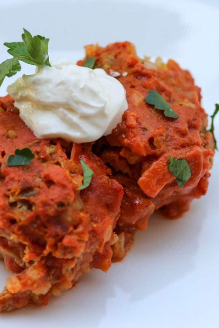 Two lazy cabbage rolls in tomato sauce with a dollop fo sour cream and chopped fresh parsley.