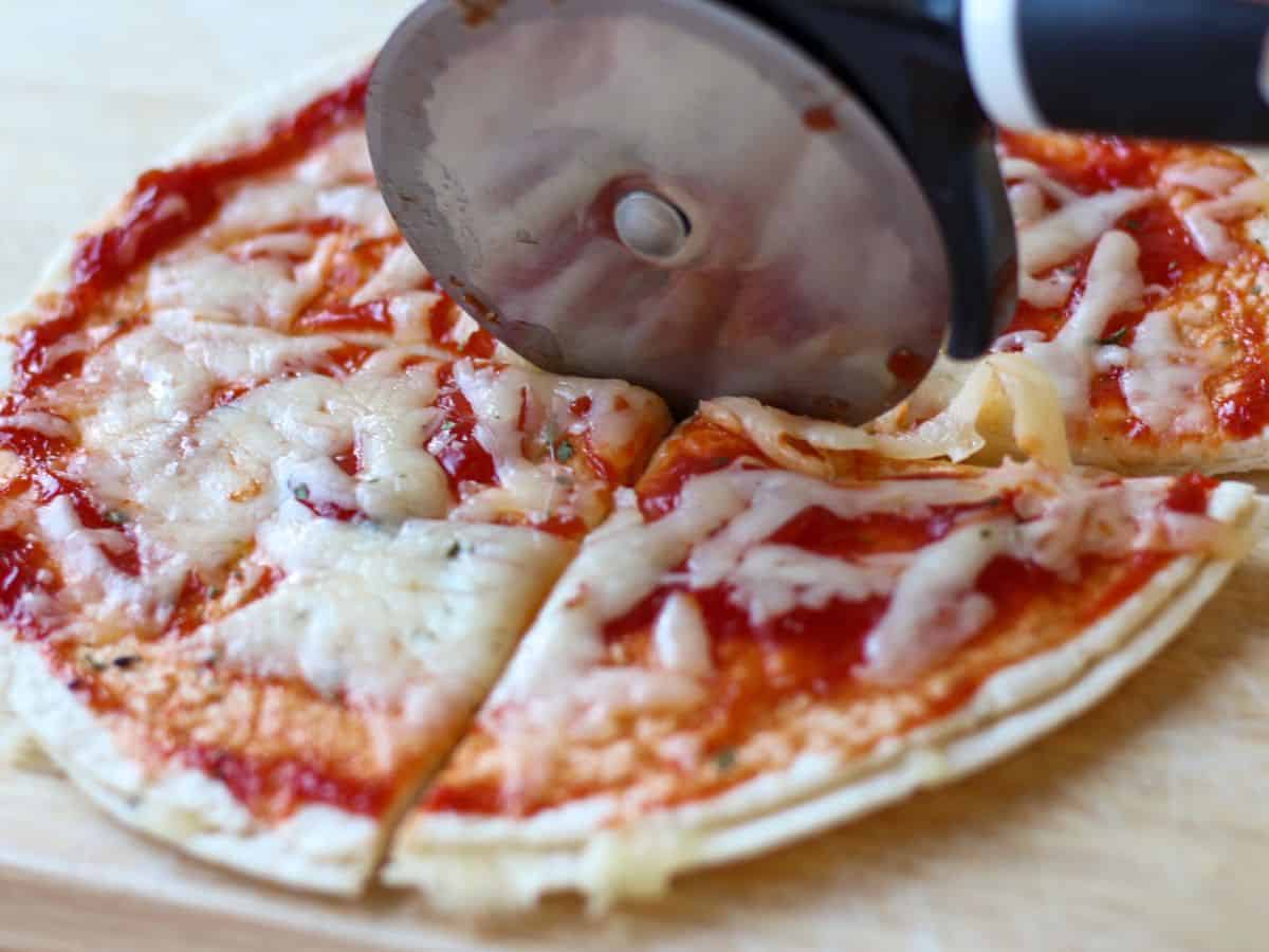 Cheese and sauce pizza is cut with a pizza cutter.