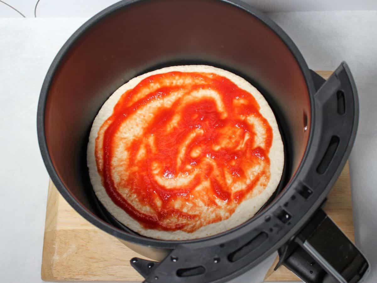 Air fryer basket with a tortilla covered in a thin layer of red sauce.