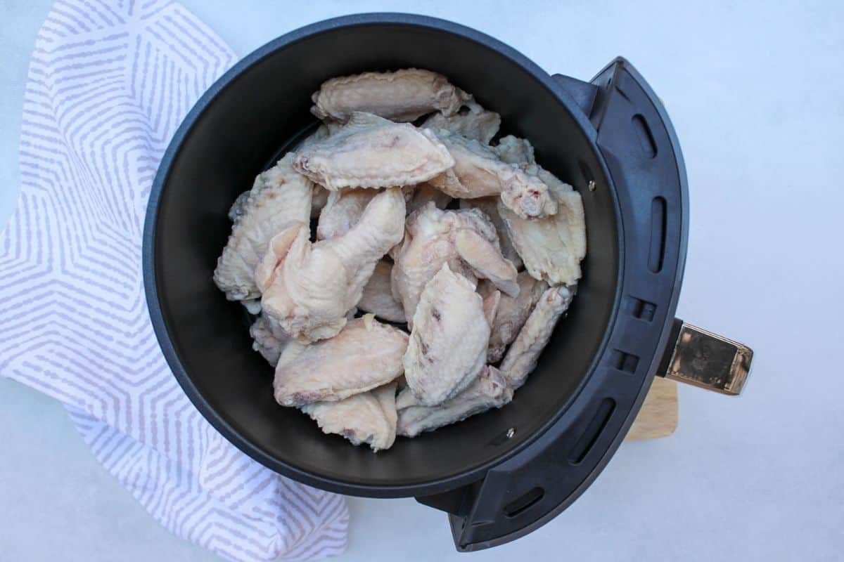 Process shot #1: raw frozen chicken wings loaded in the air fryer basket.