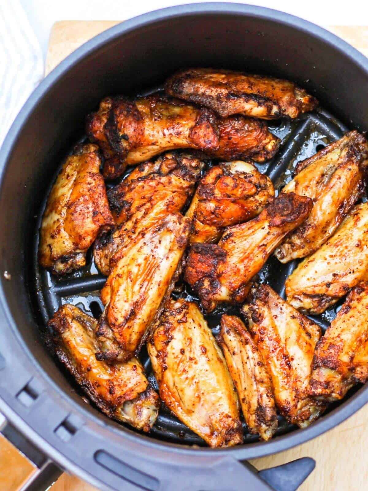 Overhead shot of air fryer basked with already cooked golden-brown wings.